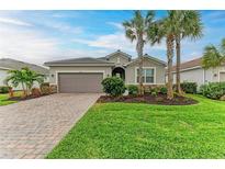 Single-story home with a paved driveway, lush lawn, and palm trees at 15169 Spanish Point Dr, Port Charlotte, FL 33981