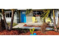 Charming house with a blue door and yellow chairs on the porch, surrounded by tropical landscaping at 18086 Clanton Ave, Port Charlotte, FL 33948