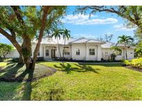 White two-story house with metal roof, landscaping, and large trees at 7563 Albert Tillinghast Dr, Sarasota, FL 34240