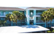 Building exterior, featuring light teal paint, palm trees, and covered parking at 19375 Water Oak Dr # 203, Port Charlotte, FL 33948
