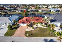 Waterfront home featuring a brick driveway, well-manicured lawn, palm trees, and a vibrant red roof at 2240 Via Esplanade, Punta Gorda, FL 33950