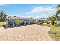 Cute bungalow with paver driveway, lush landscaping, and a bright yellow door at 351 S Mccall Rd, Englewood, FL 34223