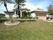 Charming home featuring a two-car garage, well-manicured lawn, and decorative landscaping with palm trees at 1247 Petronia St, North Port, FL 34286