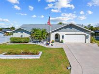 Charming single-story home with a well-manicured lawn, palm trees, and an American flag at 18326 Burkholder Cir, Port Charlotte, FL 33948