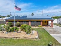 Charming one-story brick home with solar panels, an American flag, landscaped yard, and a welcoming entrance at 530 Lakemont Nw Ave, Port Charlotte, FL 33952