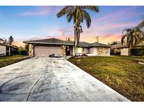 Single-story home with concrete driveway, two car garage, stone accents, and mature landscaping at 26166 Paysandu Dr, Punta Gorda, FL 33983