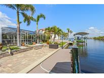 Waterfront home featuring a private dock, boat lift, and outdoor patio surrounded by lush landscaping and palm trees at 5196 Early Ter, Port Charlotte, FL 33981