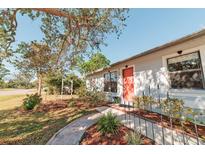 Charming house with a landscaped front yard, featuring a red door and mature tree at 700 Coquina Ct, Nokomis, FL 34275