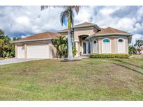 Tan house with three-car garage, palm trees, and landscaped lawn at 17164 Canary Ln, Port Charlotte, FL 33948