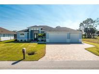 3-car garage, light blue house with gray roof, paver driveway, and landscaped lawn at 275 Broadmoor Ln, Rotonda West, FL 33947