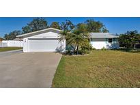 White house with teal accents, lush lawn, and a two-car garage at 450 Blackburn St, Englewood, FL 34223