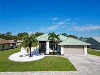 Single-story home with a green metal roof, palm trees, and white rock landscaping at 19782 Midway Blvd, Port Charlotte, FL 33948