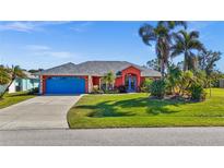 Bright coral house with blue garage door, lush landscaping, and palm trees at 62 Marker Rd, Rotonda West, FL 33947