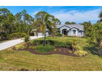 Charming home featuring a well-manicured lawn, lush tropical landscaping, and a gray exterior paint at 9350 Loyola Ave, Englewood, FL 34224