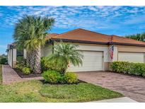 Well-maintained house with a two-car garage, lush landscaping, and a brick paved driveway at 9852 Haze Dr, Venice, FL 34292