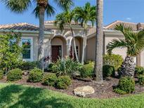 Tan one-story house with lush landscaping, red door, and palm trees at 523 Sawgrass Bridge Rd, Venice, FL 34292