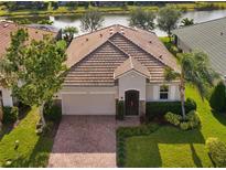 One-story home with tile roof, brick driveway, and landscaped lawn. Water view at 2049 Mesic Hammock Way, Venice, FL 34292