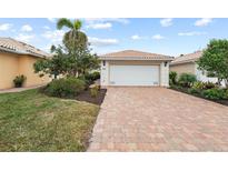 Tan two-car garage villa with paver driveway, landscaping, and walkway at 13364 Dimarco St, Venice, FL 34293