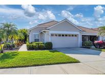Tan house with two-car garage, lush landscaping, and a paved walkway at 1891 San Silvestro Dr, Venice, FL 34285