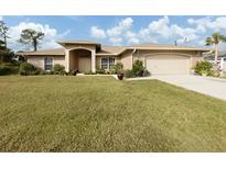 Tan house with lush lawn, attached garage, and mature landscaping at 4743 Butterfly Ln, North Port, FL 34288