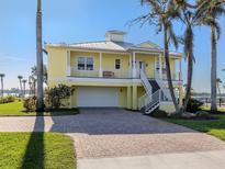 Beautiful yellow two-story home featuring a metal roof, covered balcony, and a brick driveway at 1784 Bayshore Dr, Englewood, FL 34223