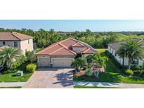 Charming single-story home with a brick driveway, tile roof, and a well-manicured front lawn with palm trees at 20590 Granlago Dr, Venice, FL 34293