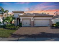 Charming home with a two-car garage, brick driveway, manicured lawn, and lush landscaping at 11903 Alessandro Ln, Venice, FL 34293