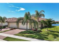 Charming home with a two-car garage, brick driveway, and lush landscaping featuring palm trees and manicured shrubbery at 24065 Canterwood Way, Venice, FL 34293