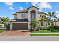 Beautiful two-story home featuring a tile roof, manicured lawn, and lush tropical landscaping at 12279 Canavese Ln, Venice, FL 34293