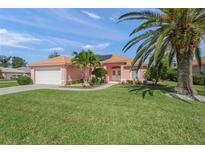 Charming pink single-story home with a tile roof, well-manicured lawn, and mature palm trees at 1904 Canary Island St, Venice, FL 34292