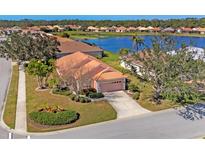 Charming single-story home featuring a tile roof, lush landscaping, and a serene lake view at 805 Derbyshire Dr, Venice, FL 34285