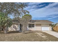 House exterior featuring a one-story light beige house with a white garage door and manicured lawn at 5405 Mariner Blvd, Spring Hill, FL 34609