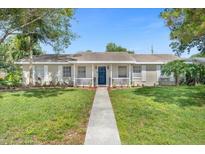 Charming home featuring a brick façade porch, blue door, and a well-manicured front yard with mature trees at 1390 Eastfield Dr, Clearwater, FL 33764