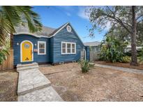 Charming blue bungalow with a yellow door, stone pathway, and manicured yard at 1143 13Th N St, St Petersburg, FL 33705