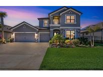 Beautiful two-story gray home with a three-car garage, stone accents, a well manicured lawn, and lush landscaping at 4606 Pond Brook Ct, Bradenton, FL 34211