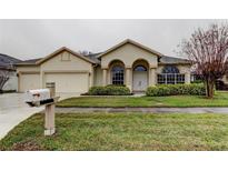 Tan house with three-car garage, arched entryway, and manicured landscaping at 28703 Hanging Moss Loop, Wesley Chapel, FL 33543