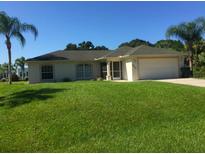 Charming single-story home with a lush green lawn, palm trees, and a two-car garage at 4666 Laramie Cir, North Port, FL 34286