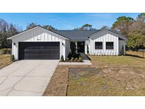 Modern farmhouse exterior boasts a white exterior, dark garage door, and landscaping at 4039 Meadow Run Ln, Wesley Chapel, FL 33543