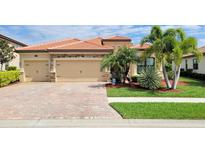 Tan house with three-car garage, paver driveway and lush landscaping at 20590 Granlago Dr, Venice, FL 34293