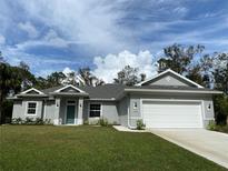 Newly constructed one-story home with gray siding, a two-car garage, and a well-manicured lawn at 7724 Swiss Ave, North Port, FL 34291