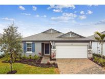 Curb appeal abounds in this charming new home; featuring a gray exterior, brick paver driveway, and lush landscaping at 5217 Patano Loop, Palmetto, FL 34221