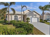 Tan one-story home with white garage door, landscaping, and palm trees at 750 Pond Lily Way, Venice, FL 34293