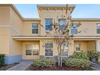 Two-story townhome with light-yellow exterior, landscaping, and walkway at 37658 Aaralyn Rd, Zephyrhills, FL 33542