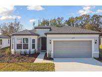 Single-story home with gray siding, two-car garage, and landscaping at 1279 Kazaz Ct, Zephyrhills, FL 33540