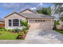 Tan one-story house with a two-car garage and landscaped front yard at 10922 Brucehaven Dr, Riverview, FL 33578