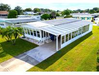 Mobile home with large sunroom and carport, situated on a spacious lot with lush lawn at 15 Hamilton Ln # 7, Palm Harbor, FL 34684