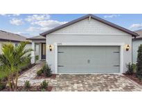 House exterior features a gray garage door, light-colored brick driveway, and walkway at 9415 Coastline Way, Parrish, FL 34219