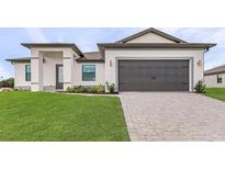 Modern home showcasing a well-kept lawn and a gray brick driveway leading to a two-car garage at 5479 Brussels Ter, Port Charlotte, FL 33981