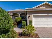 Charming front exterior showcasing a two-car garage, brick driveway, and meticulously landscaped walkway at 16233 Amethyst Key Dr, Wimauma, FL 33598