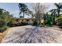 Charming yellow house with brick paver driveway, lush landscaping, and mature trees at 1747 Douglas Ave, Dunedin, FL 34698